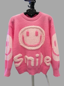 Detail of chunky knit pink sweater featuring a 3D textured white smiley face and smile text