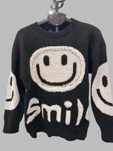 Detail of black knit sweater showing white jacquard smile pattern and smile text