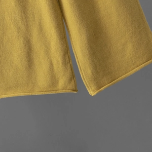 Détail du tricot jaune gingembre montrant la texture douce et la finition bord roulé