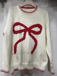 Detail of red bow jacquard and striped ribbing on off-white knit sweater
