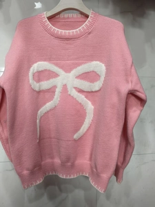 Detail of pink knit sweater showing textured white bow jacquard and white stitched trims