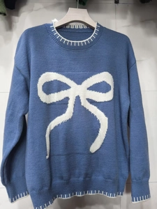 Close-up of blue crew neck sweater featuring white bow jacquard and striped hem