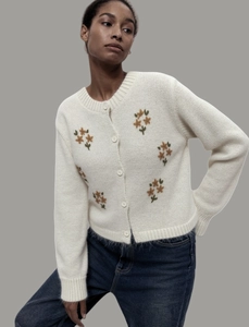 Détail du cardigan en tricot blanc avec broderie florale jaune et boutons à col rond