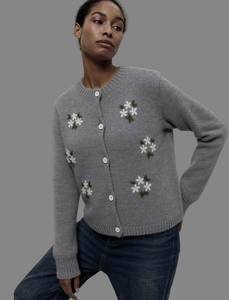 Gros plan sur un cardigan en maille pelucheuse grise avec broderies fleurs et boutons