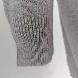 Macro shot of grey knitted sweater showing detailed ribbed cuff and premium wool texture