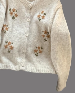 Détail de broderie florale sur gilet en maille peluche blanc crème avec boutons ronds