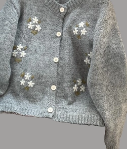 Détail du cardigan gris en tricot avec broderies de fleurs blanches et boutons nacrés
