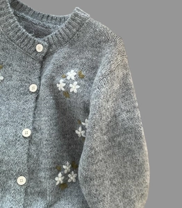 Gros plan du cardigan gris en maille avec broderies florales blanches et boutons ronds