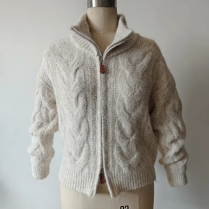 Detail of cable knit texture and metal zipper with leather pull on oat cardigan