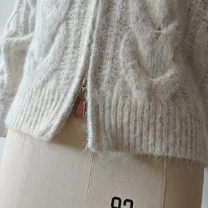 Macro shot of cable-knit alpaca texture and silver zipper detail on cream cardigan