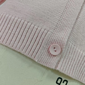 Gros plan du cardigan en maille rose montrant la texture douce et le détail du bouton