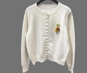 Detail of soft cream cardigan featuring hand-knitted cherry charms and ribbed cuffs