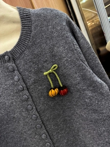 Detail of grey knitted cardigan with cherry embroidery and fabric-covered buttons