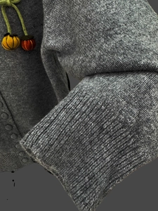 Detail of grey knit cardigan featuring handmade felt fruit pendants and ribbed cuffs