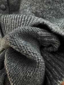 Macro detail of soft grey knit cardigan fabric with textured ribbing and matching buttons
