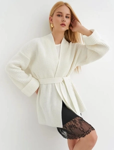 Detail of white ribbed knit cardigan featuring matching waist tie and soft cotton texture