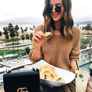 Brown oversized V-neck knit sweater with cross-back design on a beach background