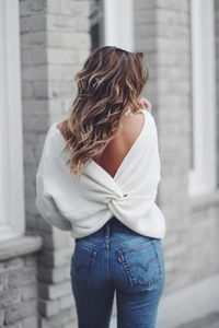 Detail shot of white knit long sleeve sweater with twist open back design and denim jeans