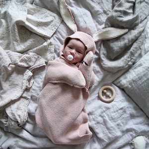 Pink knitted baby swaddle with bunny ears hood and pacifier on neutral soft bedding