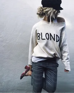 Détail d'un pull en tricot blanc cassé avec broderie BLOND et encolure décontractée à l'épaule