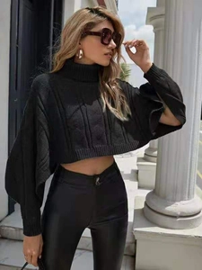 Detail of black cable knit turtleneck poncho sweater paired with matte leather trousers