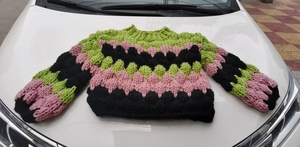 Detail of chunky handmade knit sweater featuring wavy green pink and black patterns