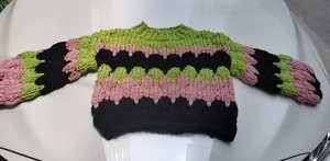 Detail of chunky handmade knit sweater featuring pink and green heart crochet patterns