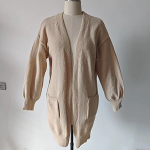 Detail of loose beige knit cardigan featuring large front pockets and ribbed cuffs