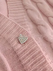 Detailed close-up of pink cable knit cardigan featuring a heart-shaped pearl button