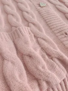 Close-up of pink cable knit sweater featuring a sweet heart-shaped pearl button detail