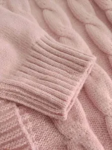 Detailed view of pink knitted cardigan showing ribbed cuffs and classic cable knit pattern