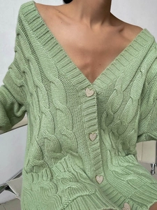 Close-up of sage green cable-knit cardigan featuring heart-shaped buttons and v-neckline