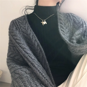 Close-up of grey cable-knit cardigan texture with a gold angel pendant necklace