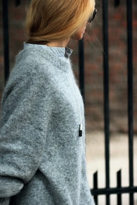 Détail du pull en maille grise avec texture duveteuse, chemise rayée et collier fin