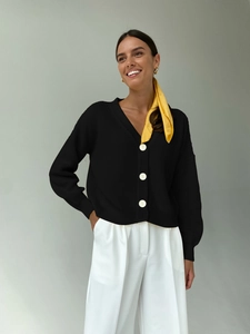 Detail of V-neck black knit cardigan with large white buttons and ribbed texture