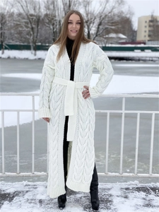 Chunky cable knit cream cardigan with matching belt and side slits in a snowy setting