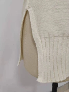 Detail eines cremeweißen Strickpullovers mit Seitenschlitz und geripptem Saum