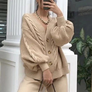 Détail de la maille torsadée et des boutons foncés sur un cardigan beige à col en V