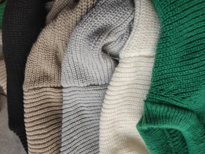Detail of ribbed knit texture on sweaters in black, khaki, gray, cream, and green colors