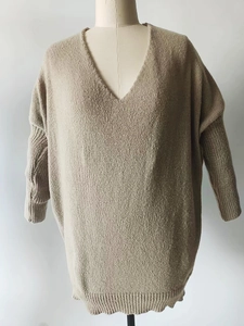 Detail view of oatmeal V-neck knit sweater featuring ribbed cuffs and loose fit texture