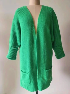 Detail einer grünen Strickjacke mit grobem Muster, Rippbündchen und aufgesetzten Taschen