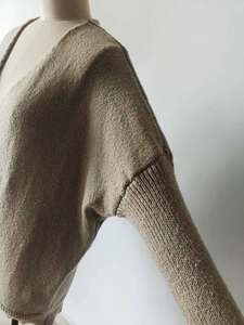 Close-up of knit fabric texture on light brown V-neck sweater with drop shoulder seam