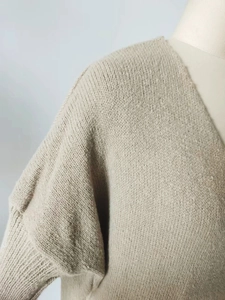 Detailed close-up of knit texture and off-shoulder seam on a beige v-neck sweater
