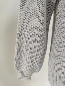 Close-up of light gray chunky knit fabric with textured stitching and ribbed lantern sleeve cuff