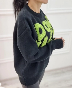 Detail of loose-fit black knit sweater featuring green embossed textured lettering