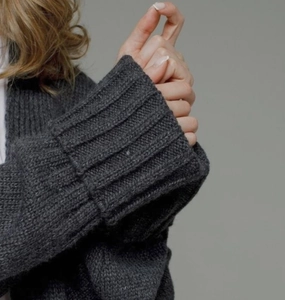 Detailed close-up of dark grey thick knit sweater sleeve with wide ribbed cuffs