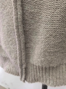 Detail of light gray chunky knit sweater showing wave texture and ribbed hem craftsmanship