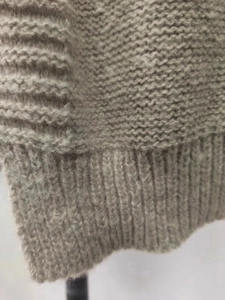 Detailed macro view of the taupe knit fabric texture and ribbed hem on the hooded sweater