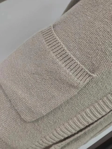 Detailed close-up of a beige hooded cardigan showing ribbed knit pockets and soft texture