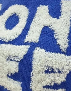 Close-up of blue knit fabric featuring white 3D chenille embroidery with letter detail